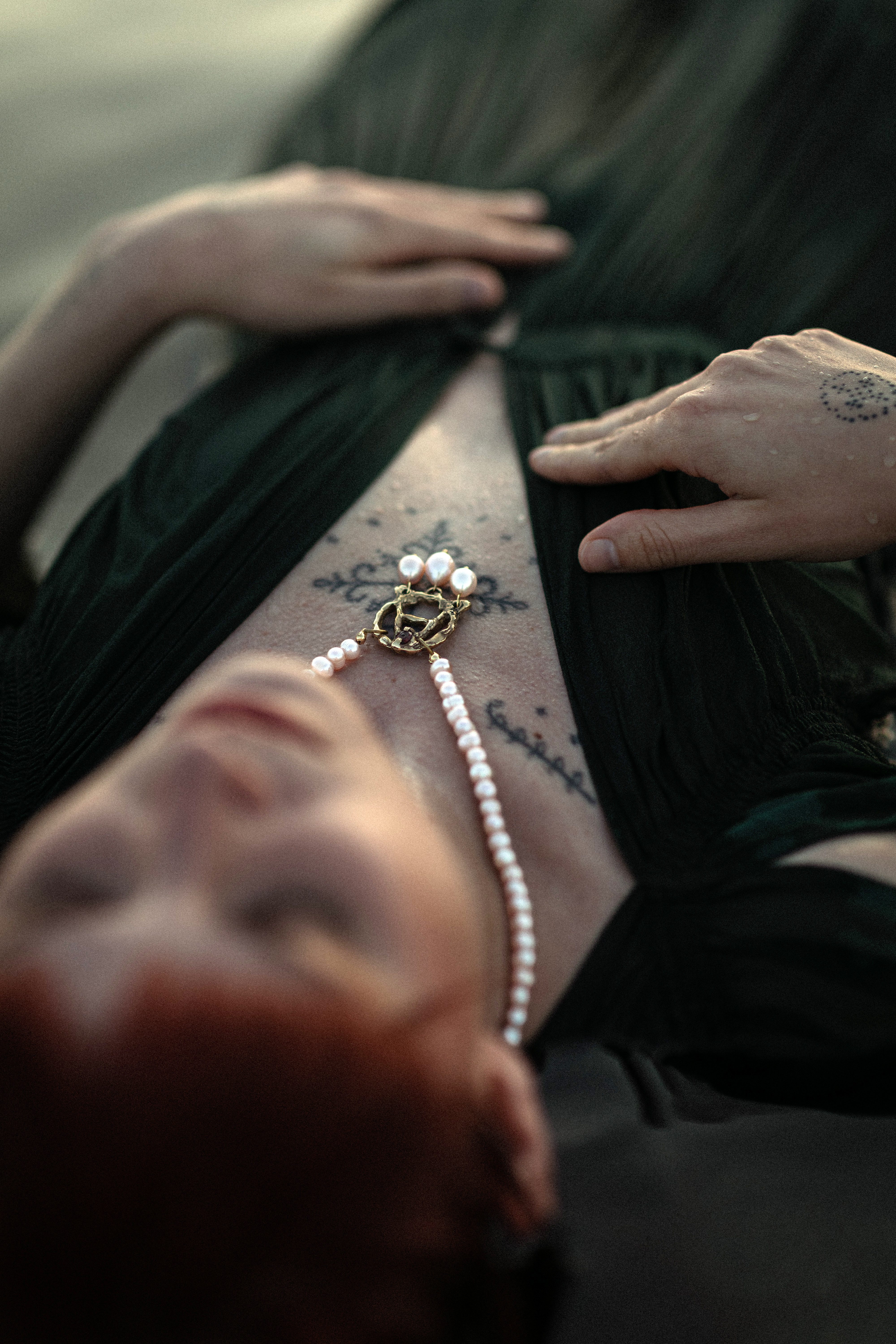 A gold and pearl talisman resting against a tattooed chest